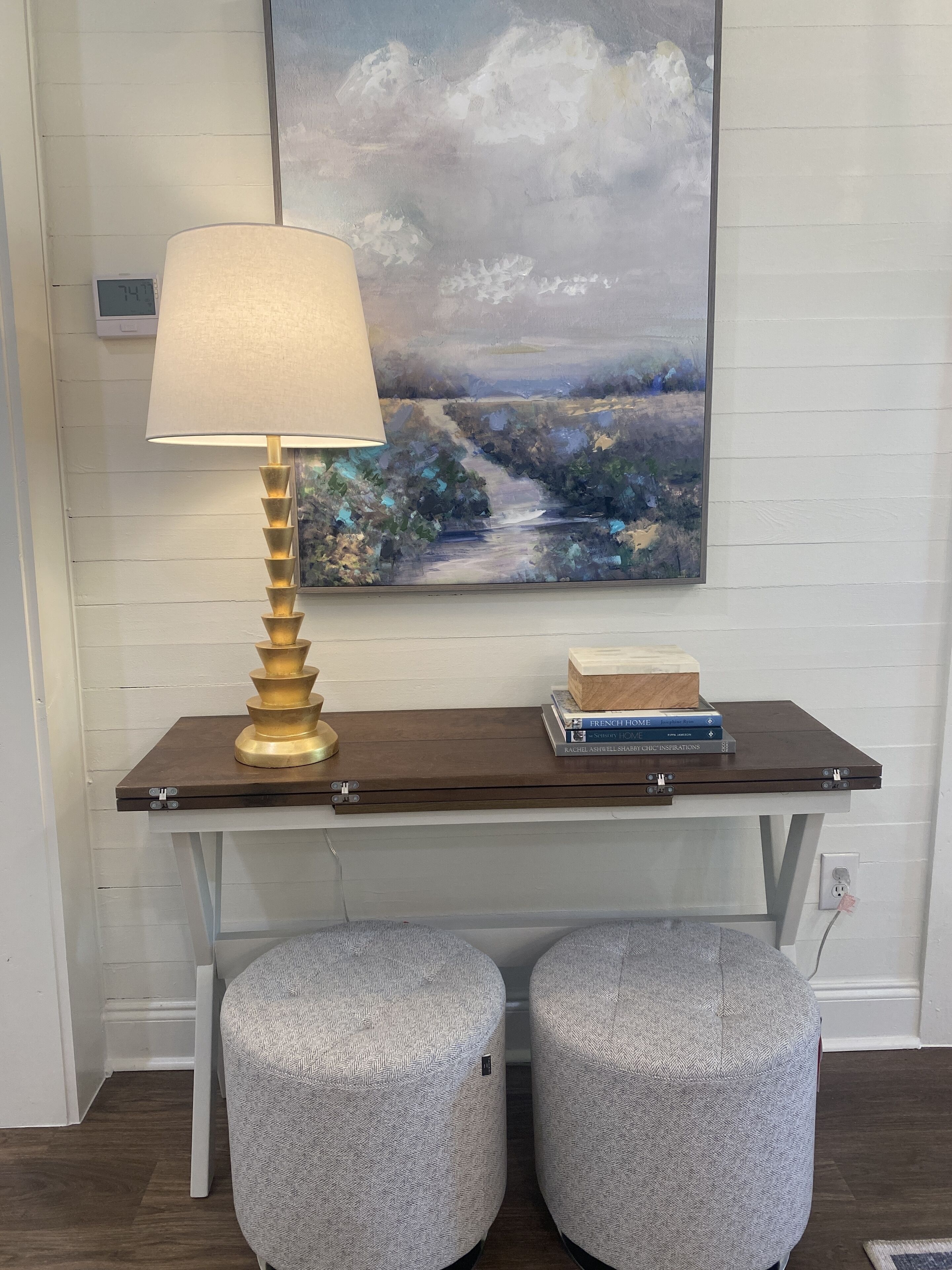 Een bureau met een lamp, boeken en een schilderij aan de muur.