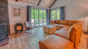 A modern living room with a wooden ceiling, large windows, a fireplace, and a leather sofa. - Modern and Brand New, Pool, Camelback Ski Area, 2 showers (Tannersville)