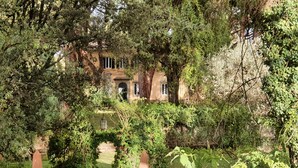 Un jardín con un camino de piedra que lleva a un edificio de fachada de piedra y ventanas arqueadas.