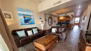 Un vaste espace de vie comprenant un canapé en cuir marron, une table basse en bois et un tableau représentant un bateau accroché au mur.
