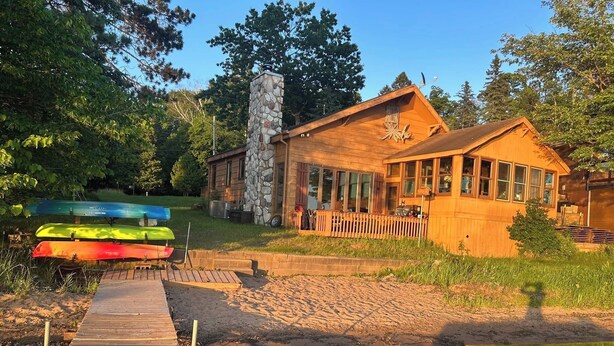 Une cabane en bois avec une cheminée en pierre, un quai et des kayaks.