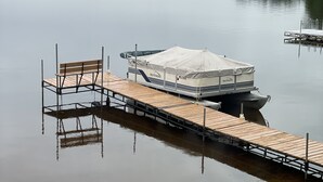 Un bateau ponton était amarré à une jetée en bois qui s’étendait dans une étendue d’eau calme. Il était doté d’un espace de repos couvert et d’un banc sur la jetée.