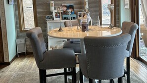 Un coin repas avec une table ronde, six chaises rembourrées, un lustre et un panneau indiquant « Bienvenue » accroché au mur.