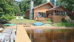 Une cabane en bois avec un quai s’avançant dans un lac paisible, le tout entouré d’une végétation luxuriante.
