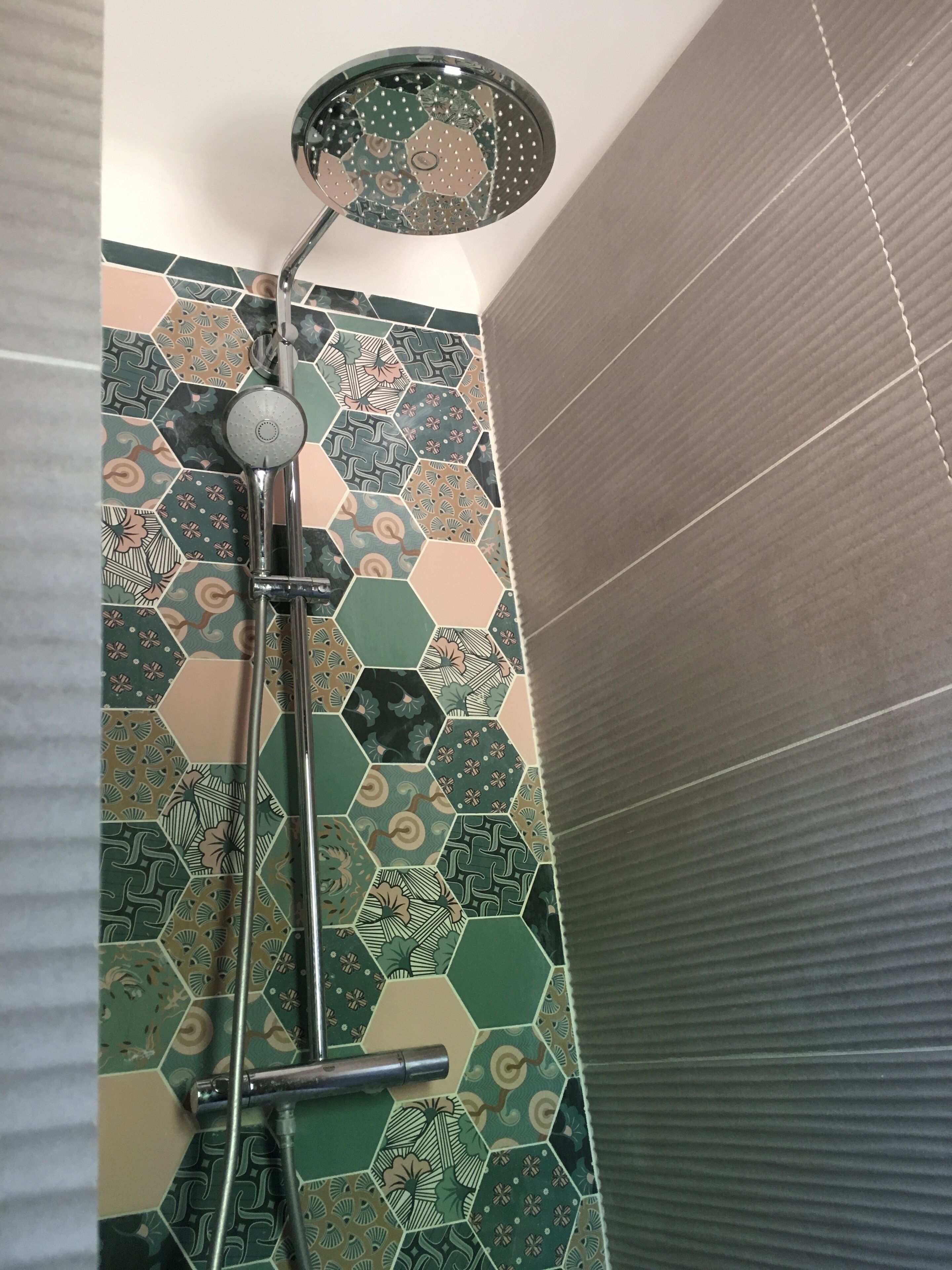 A shower with a rain showerhead and a handheld showerhead, set against a wall with hexagonal patterned tiles in various colors.