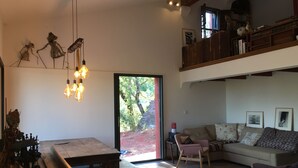 Uma sala de estar ampla com teto alto, uma mesa de jantar de madeira, um sofá e uma escada que leva a um andar superior.
