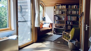 Un salon chaleureux avec un plafond en bois, une bibliothèque, un canapé et une fenêtre avec des rideaux.