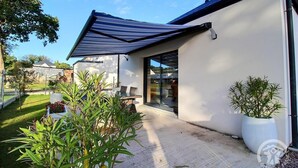 A modern house with a covered patio, a glass door leading to the interior, and a garden with potted plants. - Villa Armor Azur - ERQUY (ERQUY)