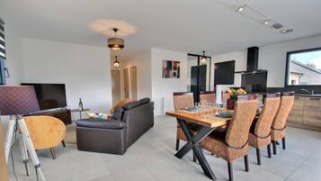 Un salon moderne comprenant un canapé, une table à manger avec des chaises, un téléviseur et une grande fenêtre.