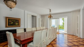 A dining room with a wooden table and white chairs, a chandelier, a framed painting, and a view through a glass door. - Beautiful home in Rab (Rab)