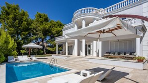 A poolside area with a pool, lounge chairs, and a covered seating area with umbrellas. - Beautiful home in Rab (Rab)