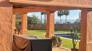 An outdoor patio with a covered grill area, stone walls, and a view of the ocean. - VILLA WITH POOL 5 MINUTES FROM THE BEACH (TORREGUADIARO)