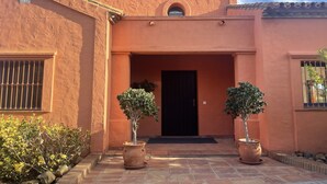A building with a red stucco exterior, a black door, and two potted trees in the entrance. - VILLA WITH POOL 5 MINUTES FROM THE BEACH (TORREGUADIARO)