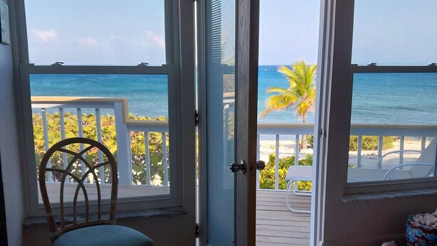 A room with a view of the ocean, a wooden chair, and a door leading to an outdoor deck.