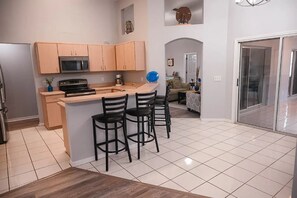 A modern kitchen with a central island, bar stools, and a microwave.