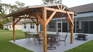 Une pergola en bois avec une table et des chaises, un foyer et un espace patio couvert.