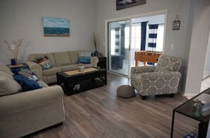 A living room with a sofa, armchair, coffee table, and a foosball table. - Spacious 4-bedroom home, just minutes from beach! (Palm Coast)
