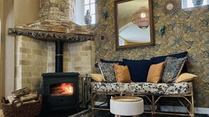 A cozy living room with a stone fireplace, a sofa with patterned cushions, a hanging light fixture, and a decorative mirror. - La Bigourdane (Gerde)