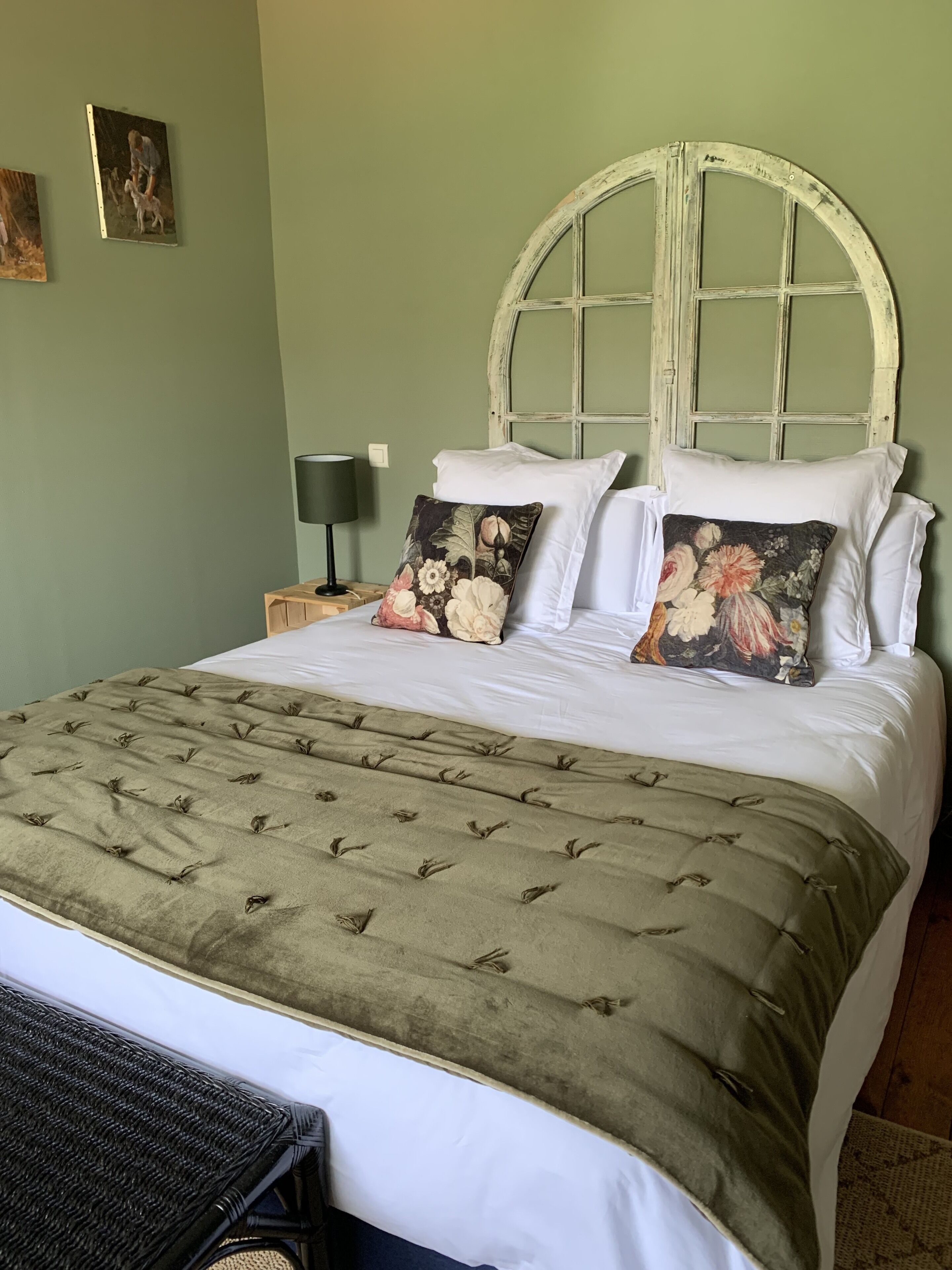 A bed with a green upholstered headboard, white bedding, and floral pillows.