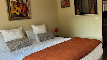 A bedroom with a large bed, two paintings, a window, and a red spherical object.