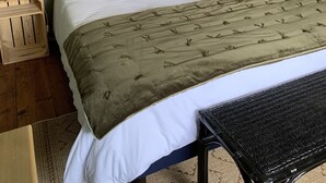 A neatly made bed with a green throw blanket, two white pillows, and a floral pillow. There are two bedside tables with lamps, a wooden headboard, and a black wicker chair. - La Bigourdane (Gerde)