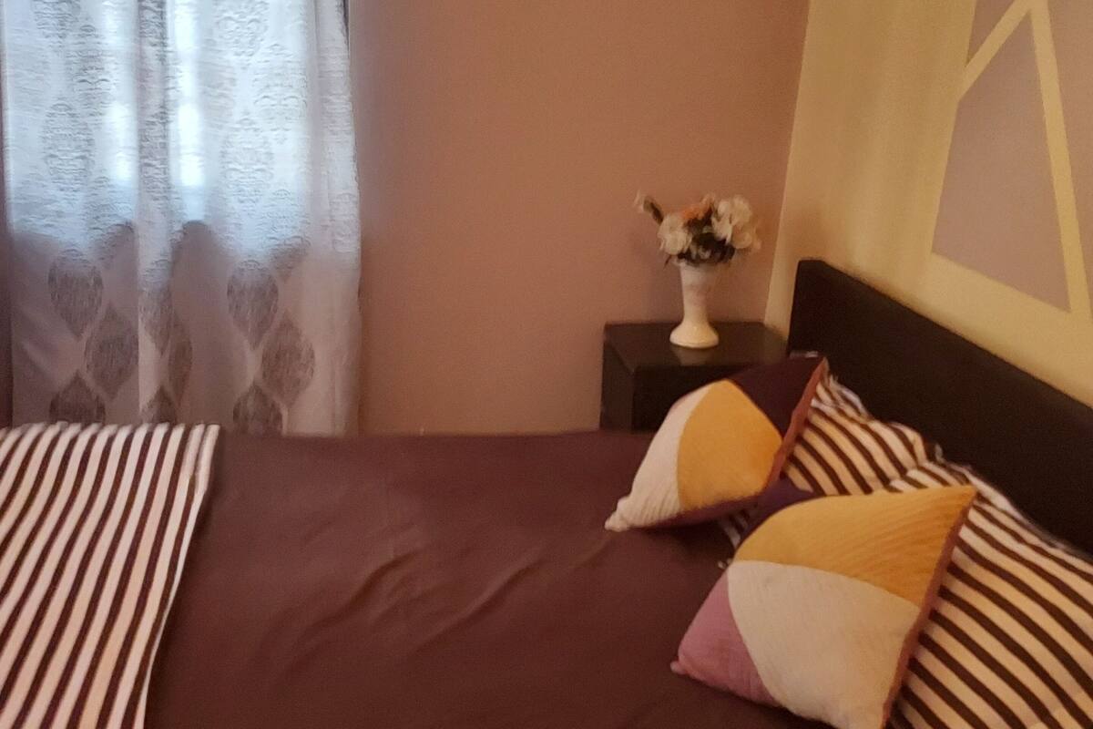 Un lit bien fait, avec une literie à rayures, un vase rempli de fleurs sur une table de chevet et une étagère avec de petites plantes.