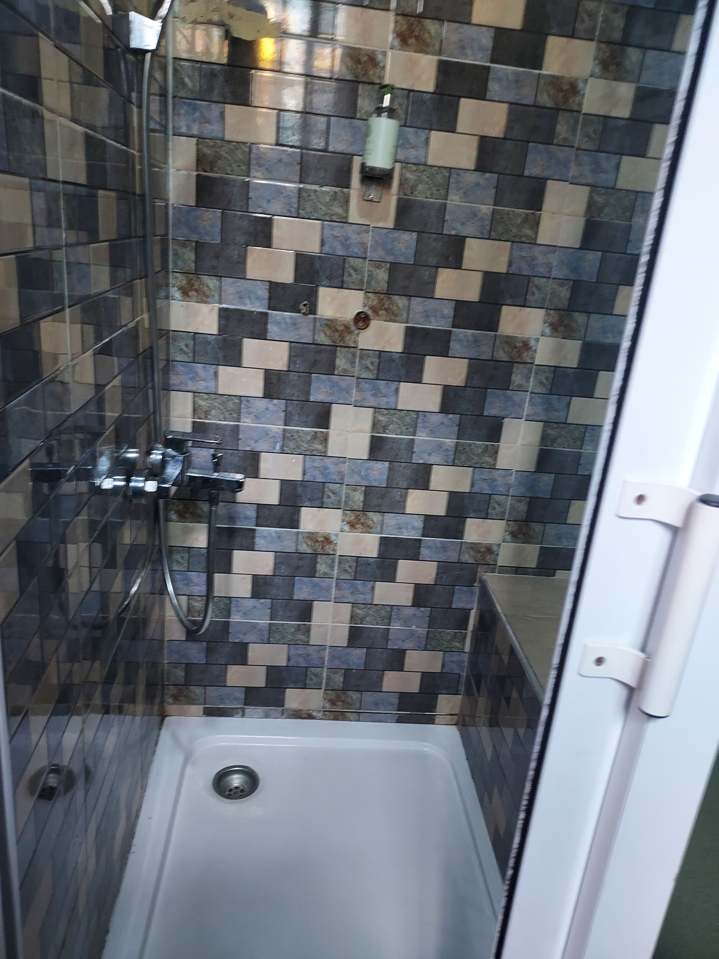 A shower with a tiled wall, a glass door, and a white bathtub.