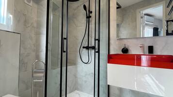 A modern bathroom with a glass-enclosed shower, a white toilet, and a red and white vanity.