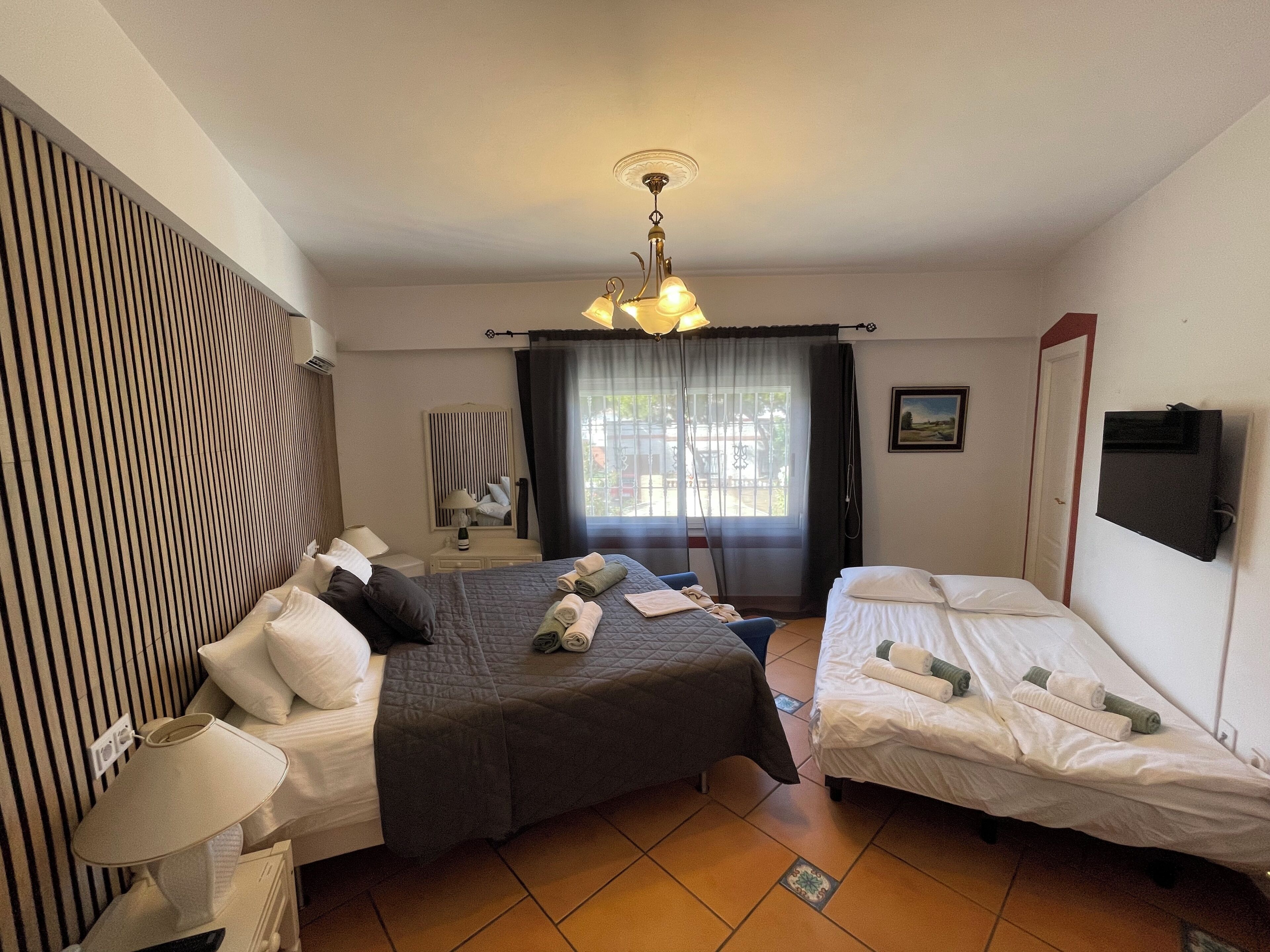 Habitación de hotel con dos camas, ventilador de techo, televisión y ventana con cortinas.