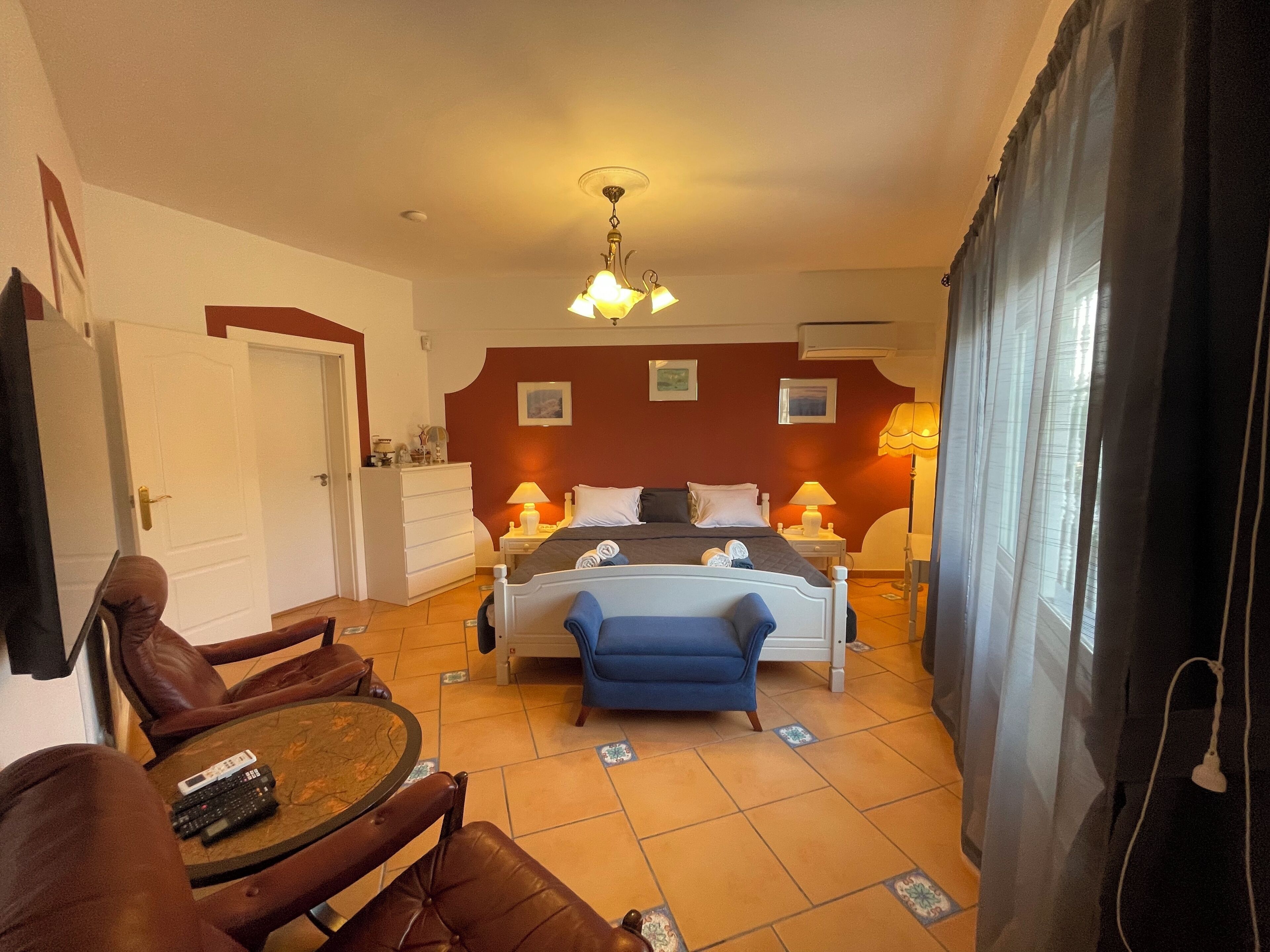 Habitación de hotel con cama, dos mesitas de noche con lámparas, una pequeña mesa con sillas y un televisor.
