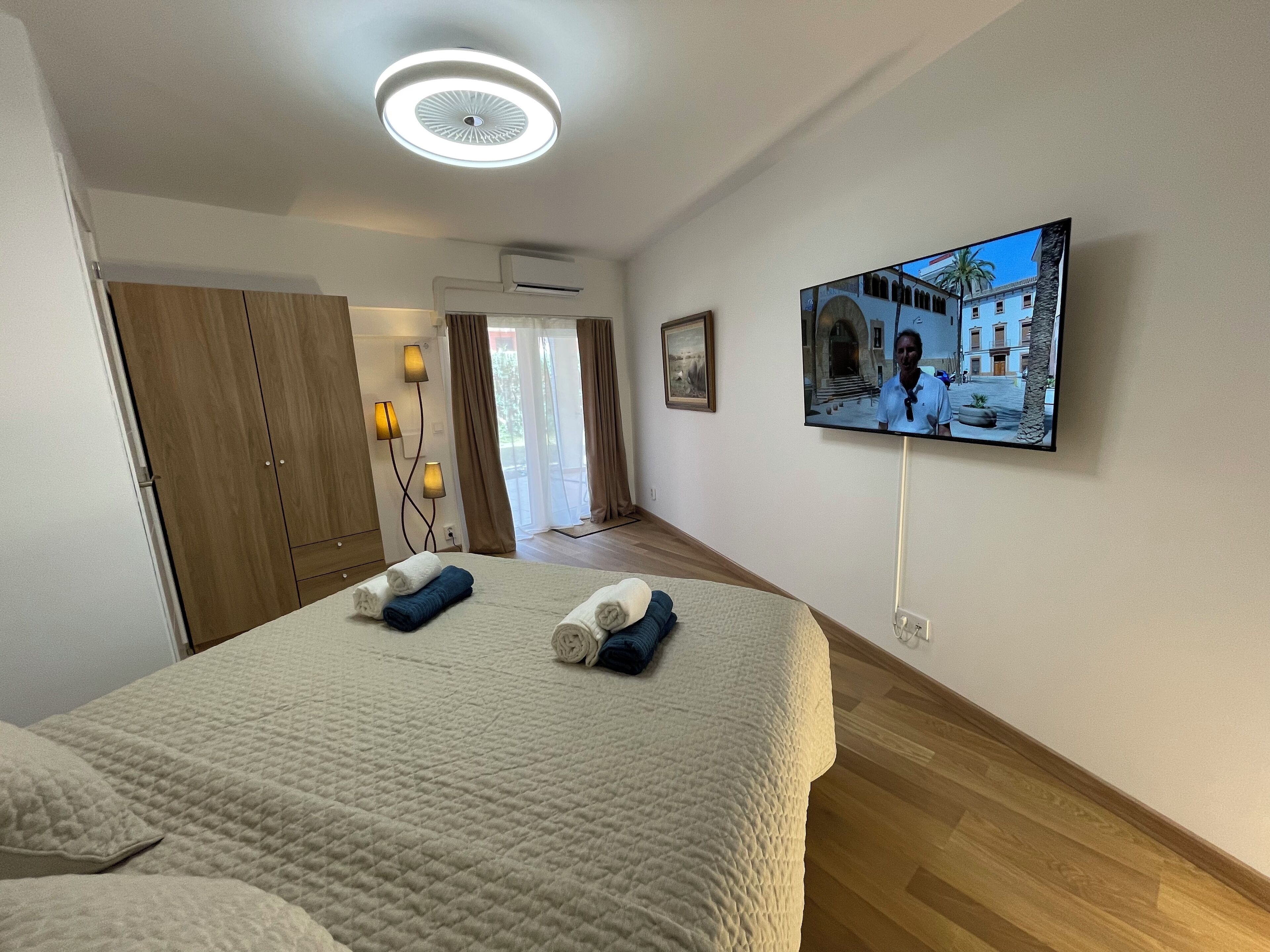 A hotel room with a bed, a TV on the wall, and a view of a building outside.