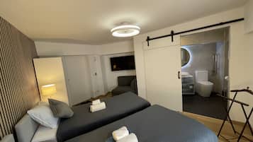 Una habitación de hotel moderna con dos camas, un televisor de pantalla plana, un espejo y un baño con inodoro y lavamanos.
