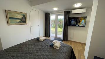 Een slaapkamer met een bed, een schilderij, een airconditioning, een televisie en een schuifdeur naar buiten.
