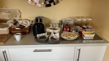 Un buffet per la colazione con un tostapane, tazze da caffè e diversi cibi su un bancone.