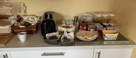 Un buffet de petit-déjeuner est installé sur un comptoir, avec un grille-pain, des tasses à café et divers aliments.