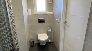 A compact bathroom with a toilet, a small window, a towel rack, and a vent.