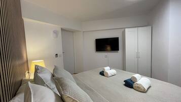 Ett hotellrum med en säng, kuddar, en tv som är monterad på väggen och en garderob.