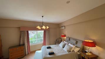 Een slaapkamer met een bed, nachtlampjes, een dressoir, een raam met gordijnen en een plafondlamp.
