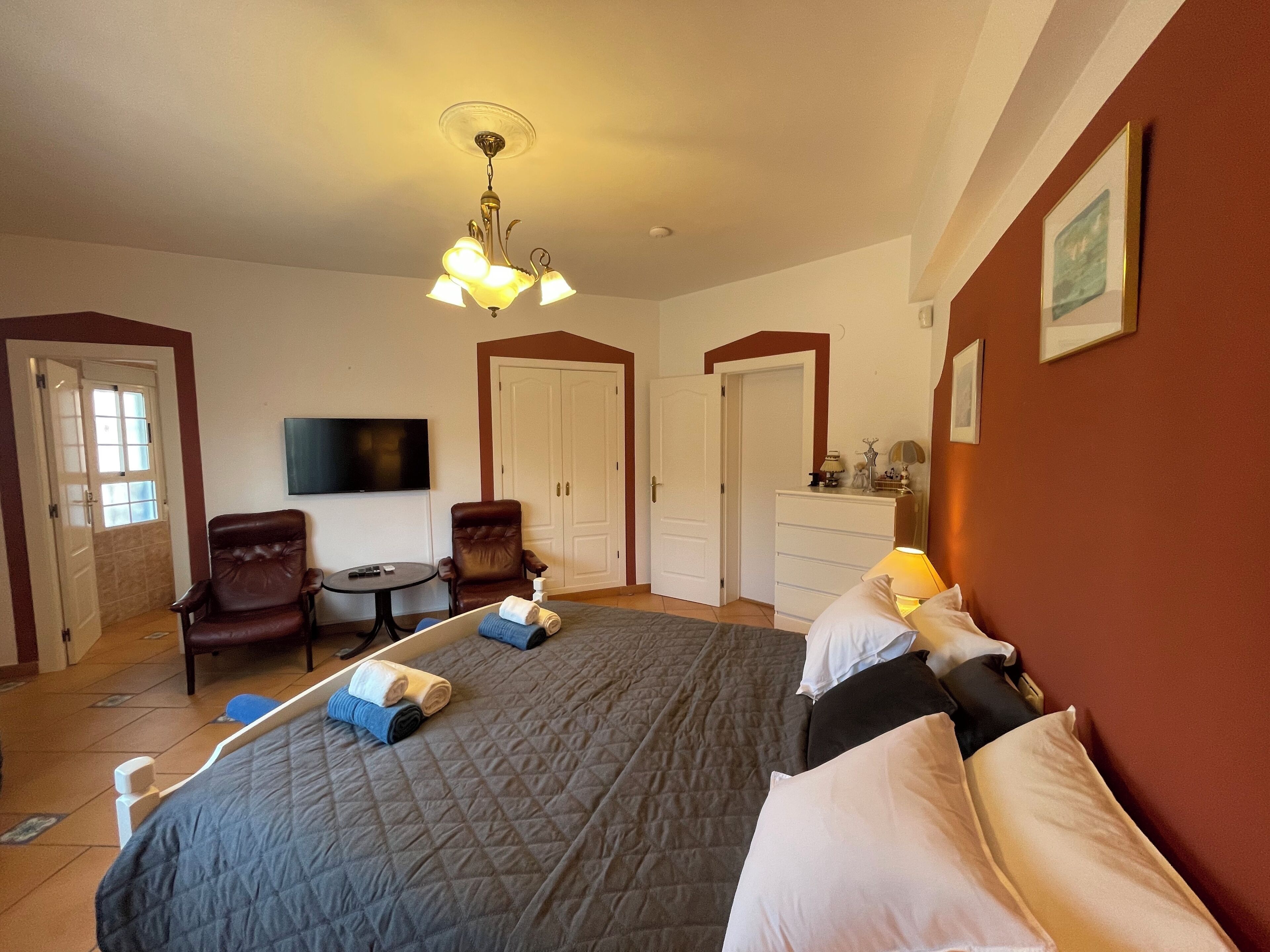 Habitación de hotel con una cama grande, un escritorio, una silla, un televisor y un armario.