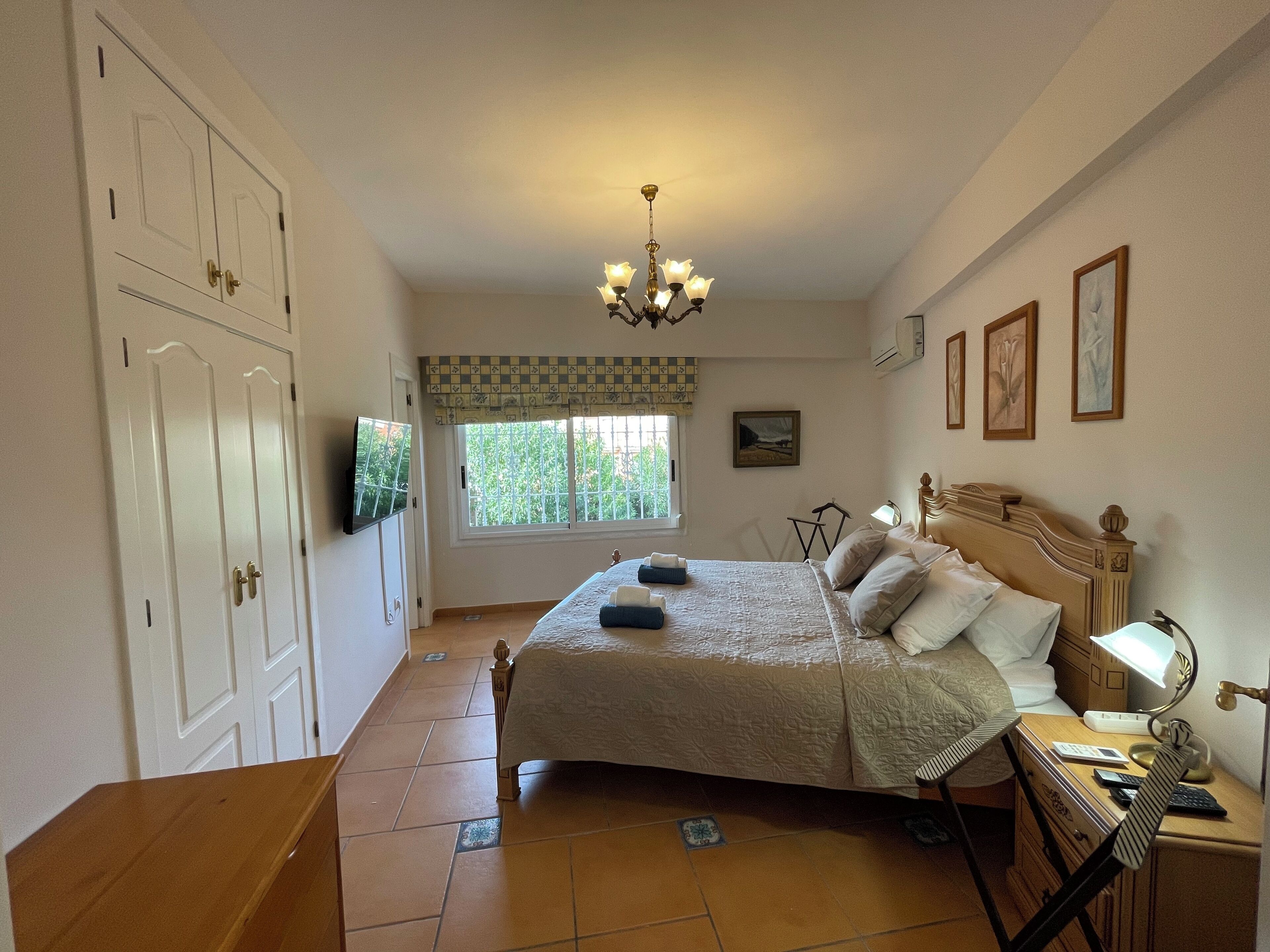 A bedroom with a bed, bedside table, lamp, and a window with a view of greenery.
