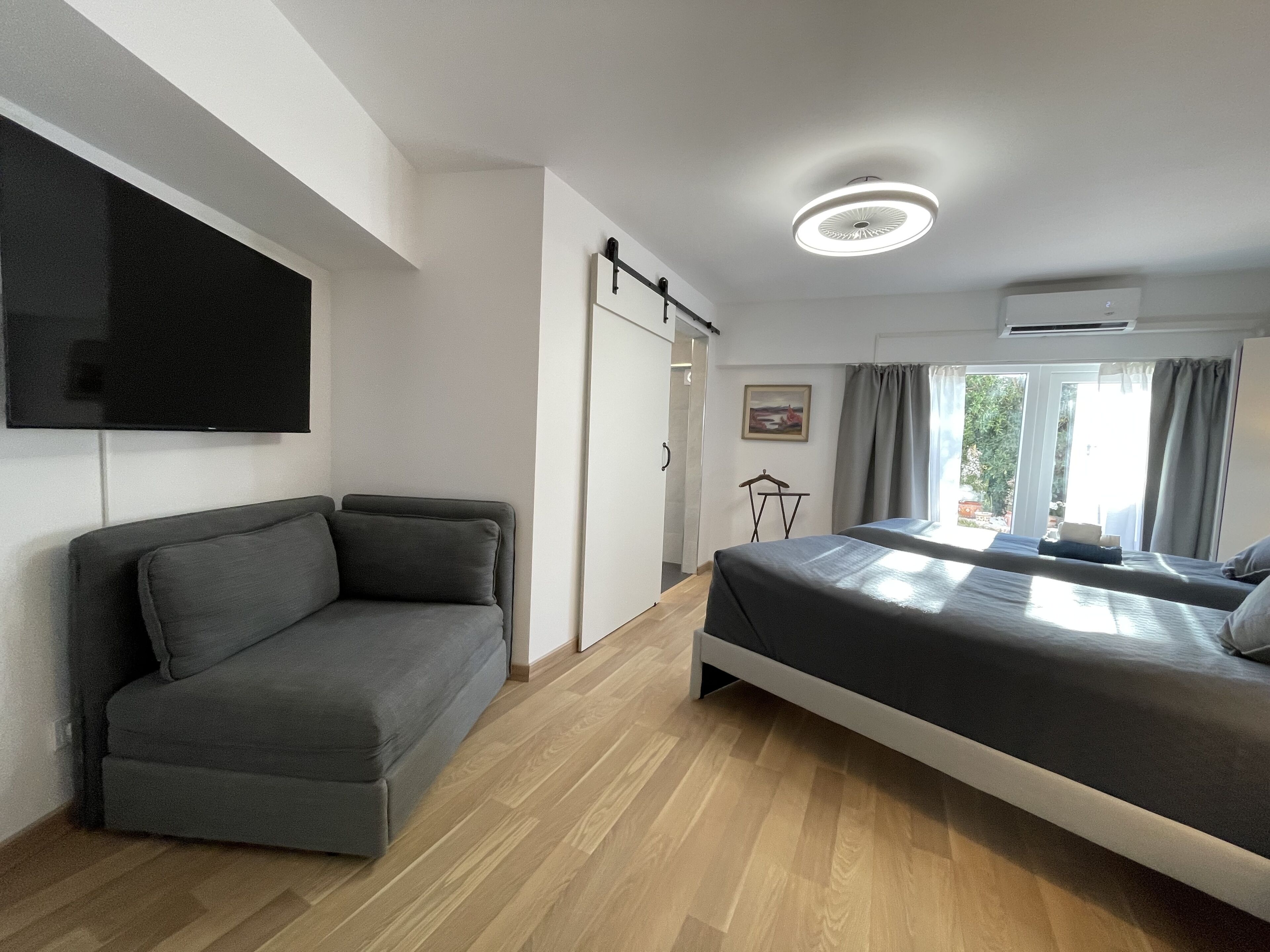 A modern hotel room with a sofa, a bed, a flat-screen TV, and a window with curtains.