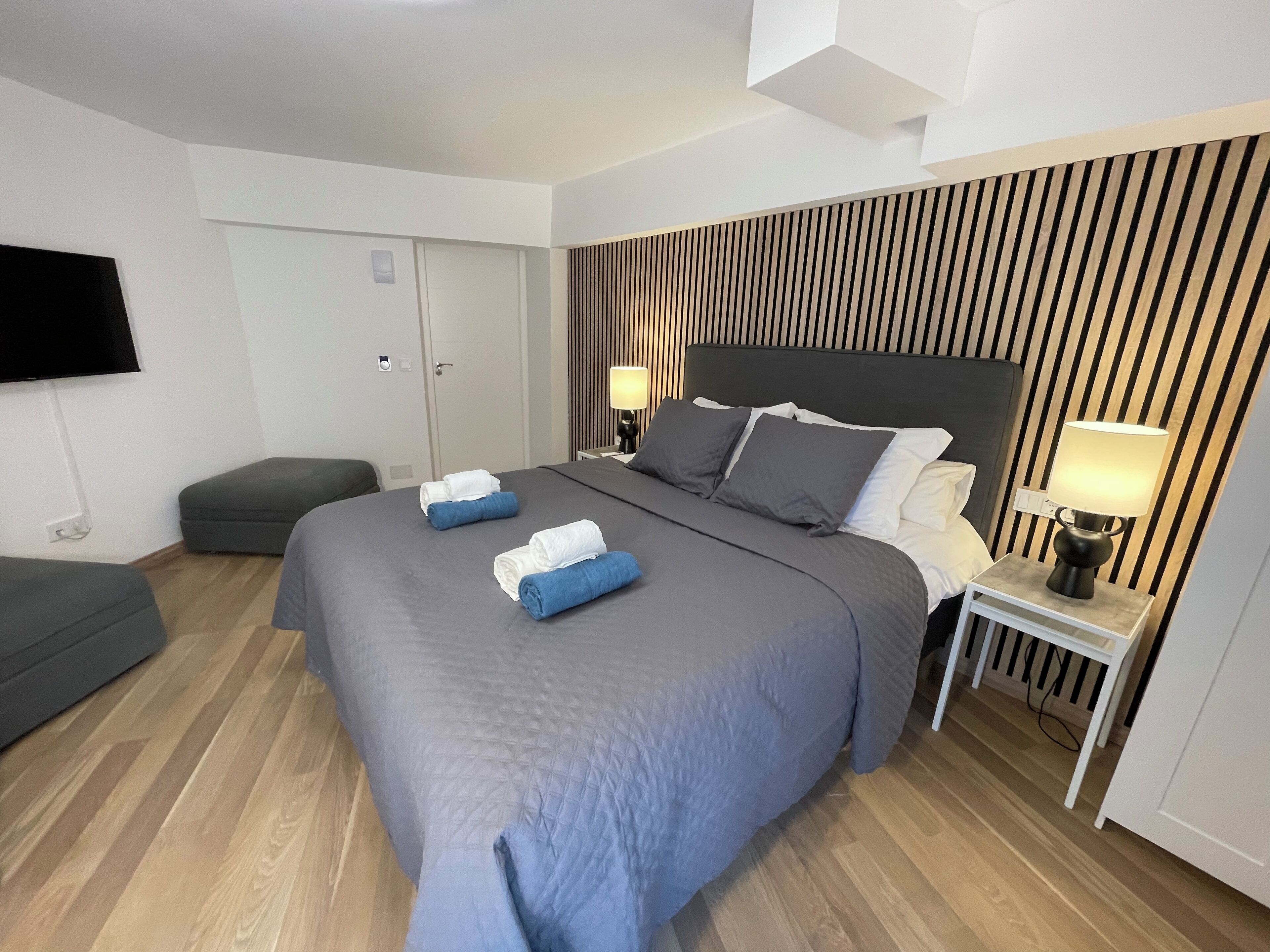 Ett modernt hotellrum med en stor säng, ett nattduksbord med en lampa, en platt-TV som är monterad på väggen och ett trägolv.