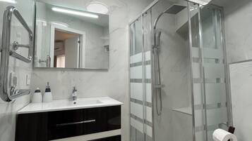 Un baño moderno con ducha envuelta en vidrio, un lavabo blanco con espejo superior y un inodoro.