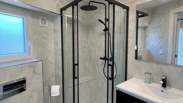 Een moderne badkamer met een douchecabine van glas, een wit wastafelmeubel en een toilet.