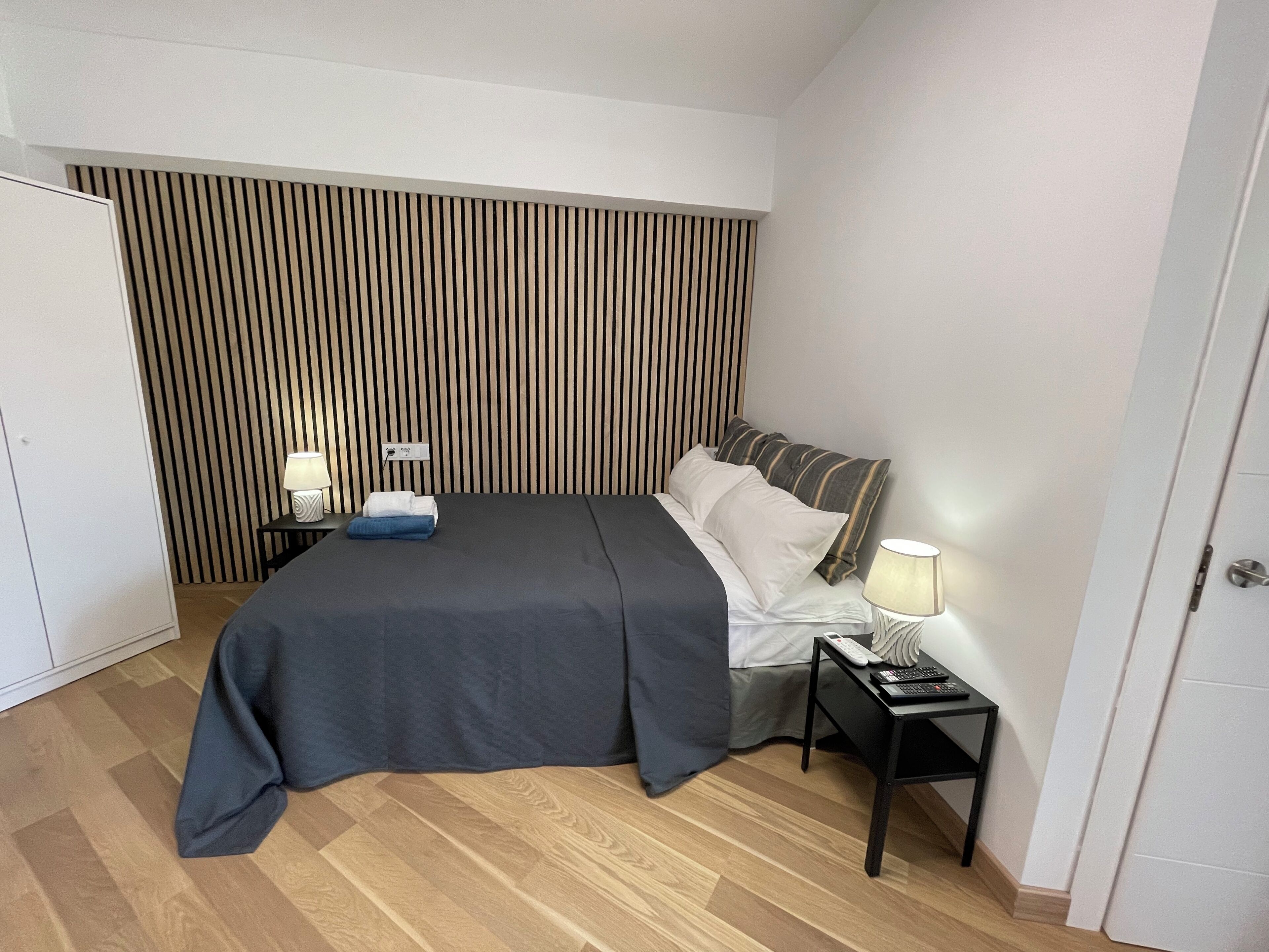 Een verzorgde hotelkamer met een bed, nachtkastjes, een lamp en een gestreept hoofdeinde.