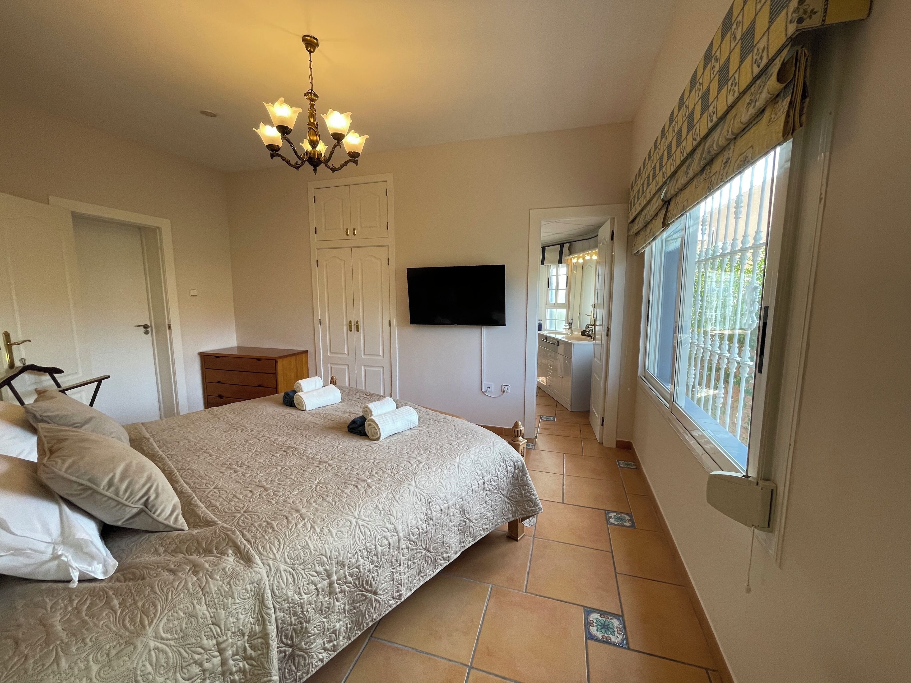 Een slaapkamer met een groot bed, een kroonluchter, een kledingkast, een televisie en een raam met uitzicht.