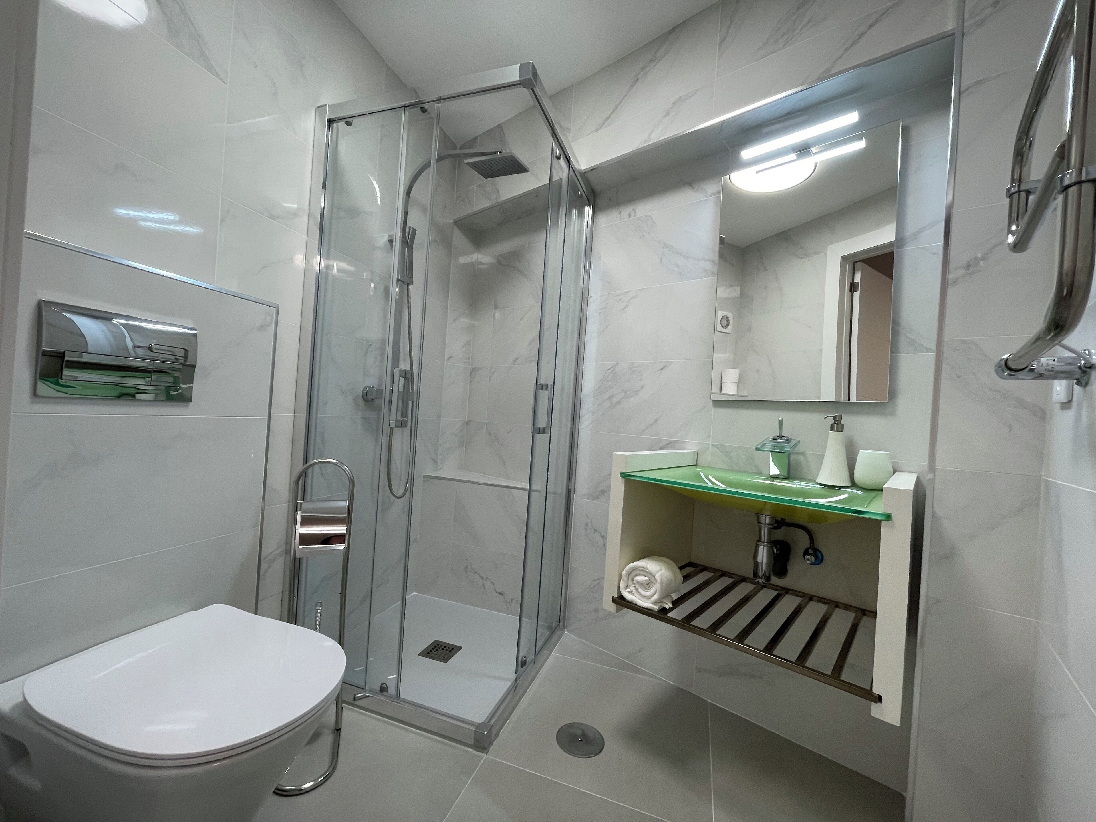 A modern bathroom with a glass-enclosed shower, a white toilet, and a green-topped sink with a mirror above.