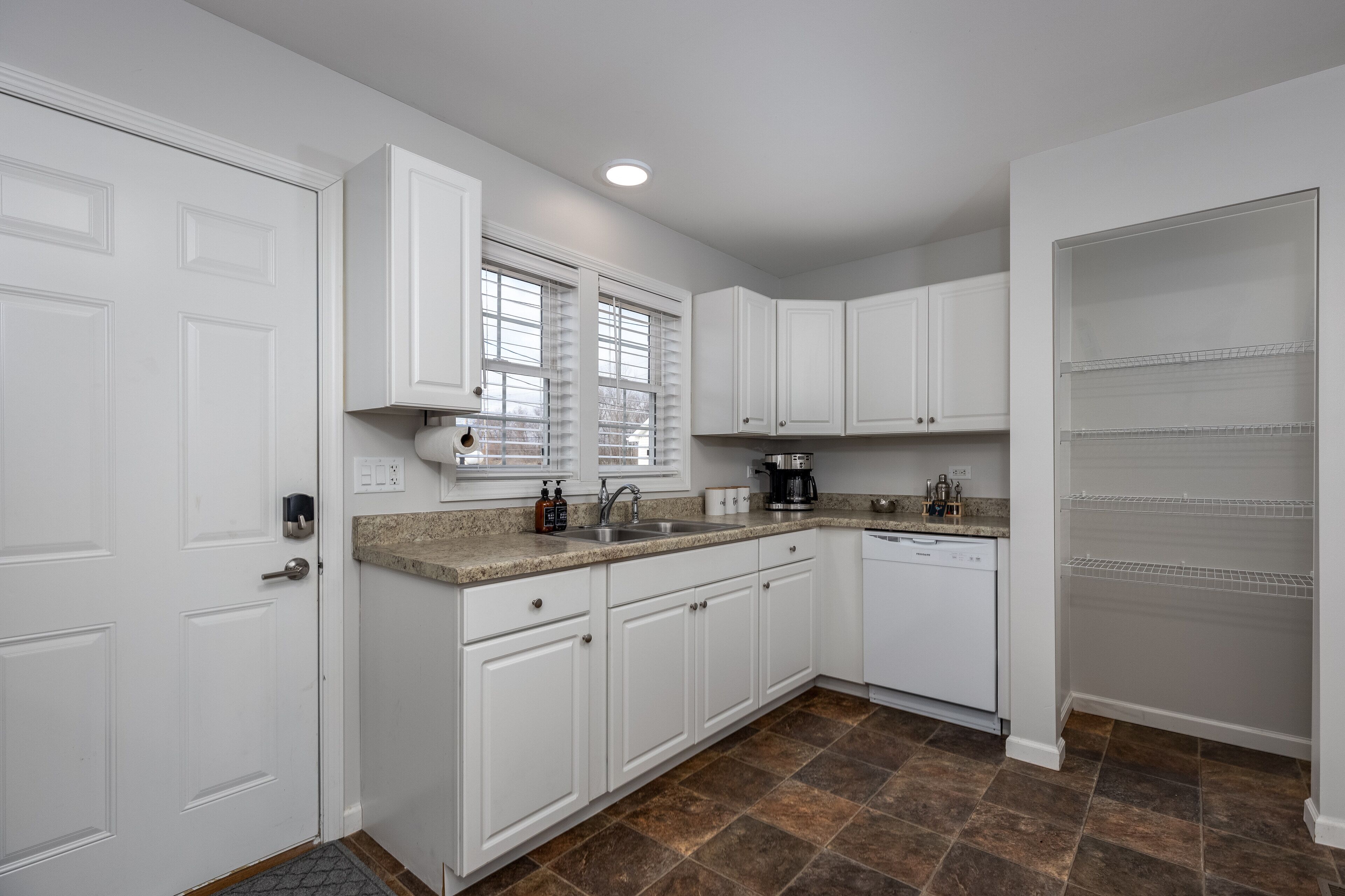 A modern kitchen with white cabinetry, a granite countertop, a built-in oven, and a dishwasher.