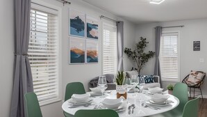 A dining area with a round table set for four, surrounded by green chairs. There are four framed artworks on the wall, a potted plant, and a sign with a motivational quote. - Starved Rock & Ottawa Retreat Amazing Getaway Home (Ottawa)