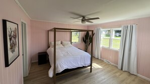 Un dormitorio con cama con dosel, ventilador de techo, ventana con cortinas e imagen enmarcadas en la pared.